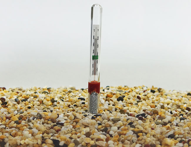 Sinking thermometer resting on gravel substrate at bottom of aquarium