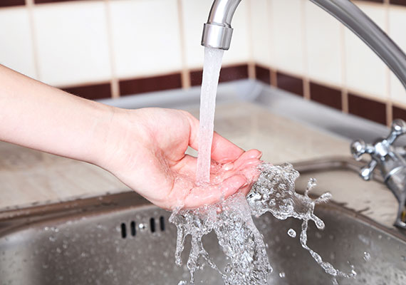 Drinking water flowing from faucet in kitchen into hand