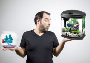 Man comparing a betta bowl that is too small to a larger sized betta tank